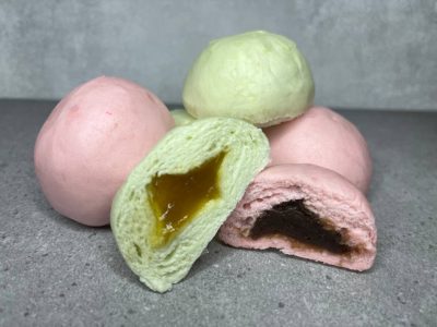 Pau mini berwarna hijau pastel dan merah jambu, sebahagian dibelah dua menunjukkan inti kaya dan inti kacang merah yang pekat, disusun bertindih. Manakal dibelakangnya, ada tiga biji pau yang disusun membentuk piramid dan satu biji ditindih didepan.