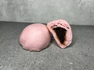 Pau mini berwarna merah jambu dengan inti kaya yang pekat, ditampilkan satu dibelah dua di sebelah satu biji pau penuh.