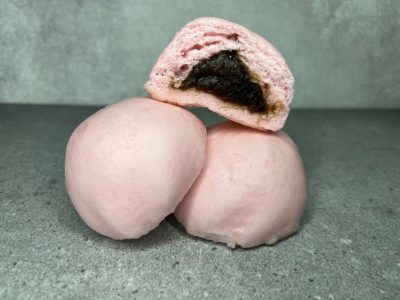 Pau mini berwarna merah jambu dengan inti kaya yang pekat, ditampilkan satu dibelah dua di atas dua biji pau penuh.